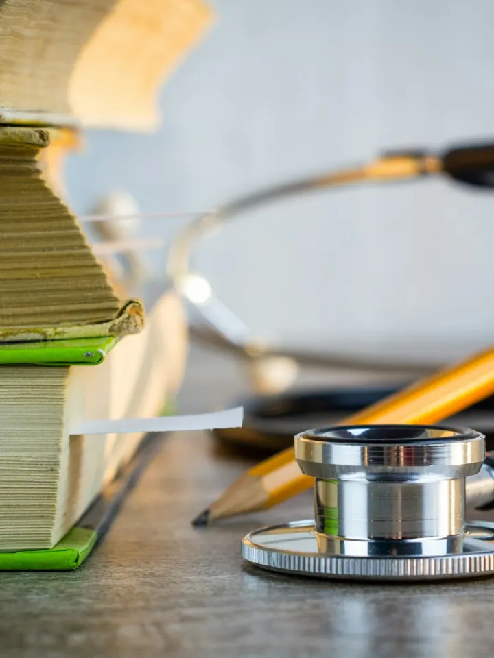 A stethoscope resting beside a stack of medical textbooks and a pencil